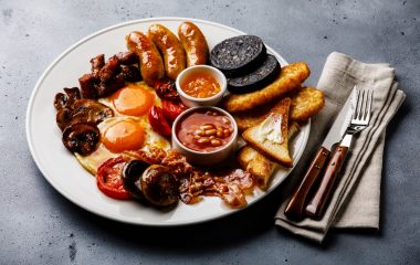 Full fry up English breakfast with fried eggs, sausages, bacon, black pudding, beans and toasts on gray concrete background